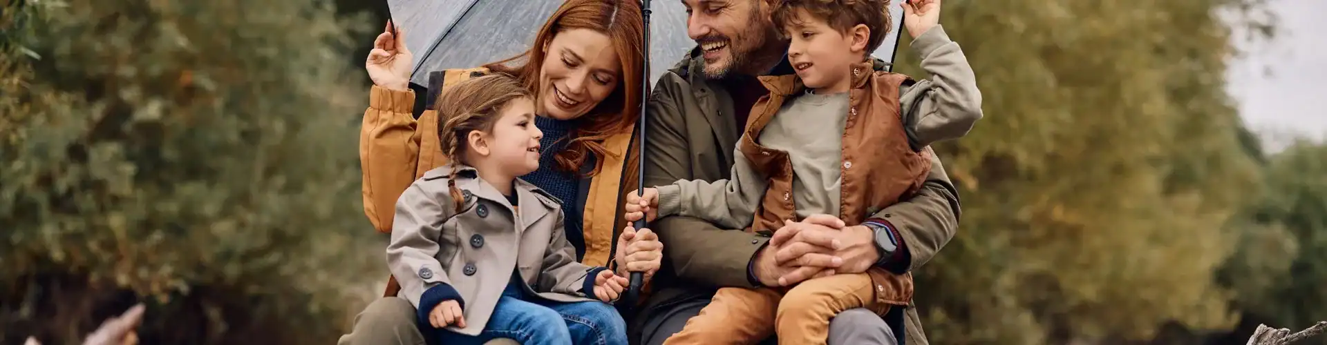 A young family sheltering under an umbrella and smiling.