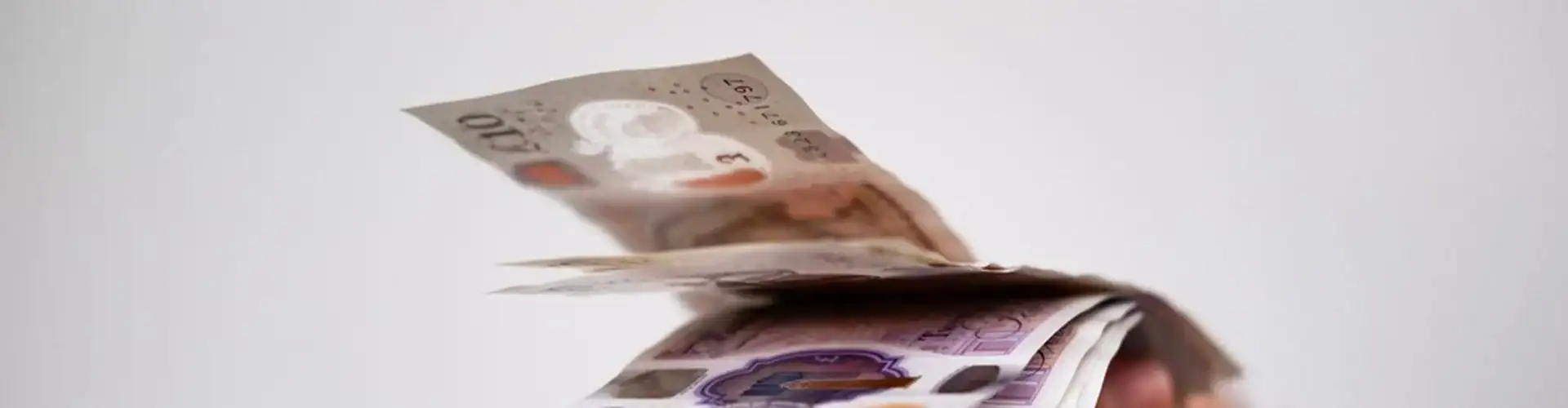 A hand holding UK bank notes.