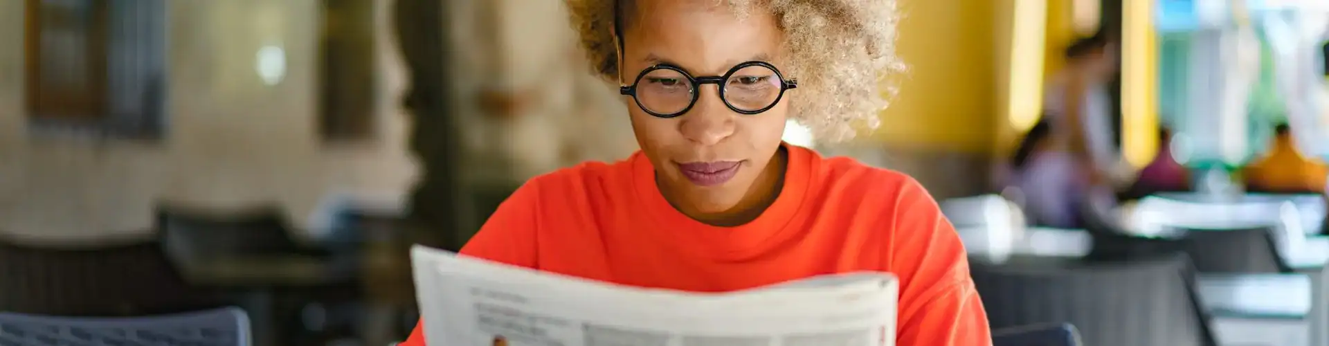 A woman reading a newspaper in a café.